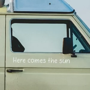 Here comes the sun sticker afgebeeld op een volkswagen surfbus ingezoomd.